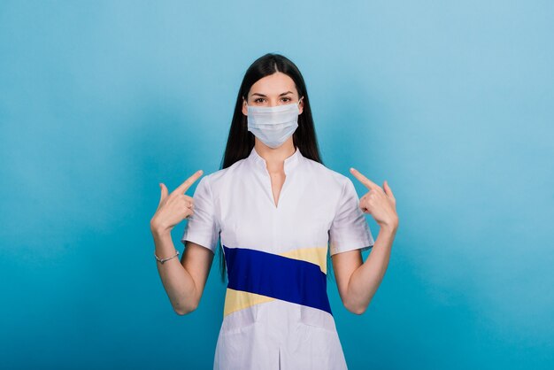 Retrato de mujer médico en una máscara médica mirando lejos aislado en azul