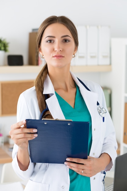 Retrato de mujer médico terapeuta de medicina en bata blanca sosteniendo el portapapeles en la oficina