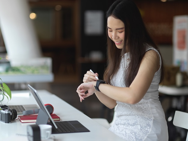 Retrato de mujer mirando smartwatch mientras trabaja en el espacio de trabajo co