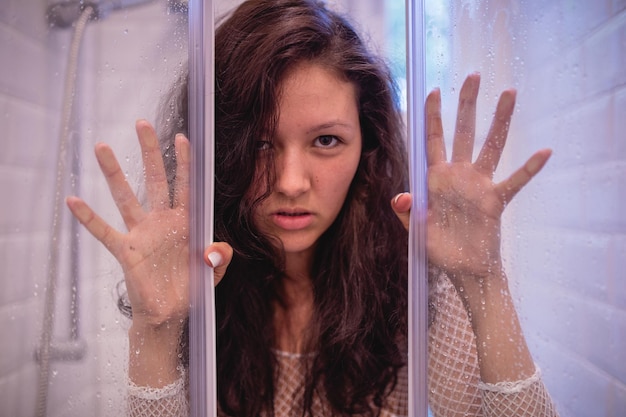 Retrato de una mujer mirando a través de una ventana de vidrio húmedo