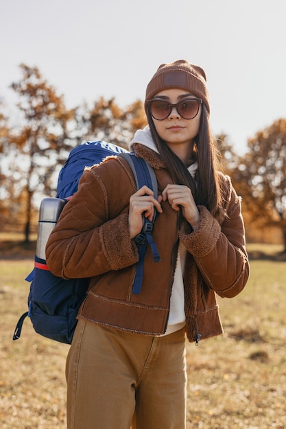 Retrato de mujer mochilera mirando a la cámara mientras está de pie contra el bosque de otoño en un día soleado