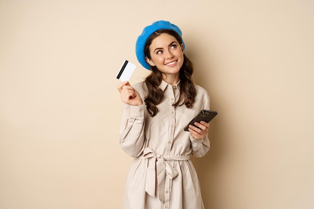 Retrato de mujer de moda en abrigo con teléfono inteligente que muestra compras con tarjeta de crédito en línea orden algo...