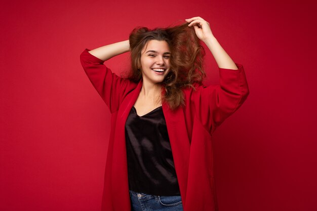 Retrato de mujer de moda alegre positiva en ropa formal mirando a cámara aislada sobre fondo rojo con espacio de copia.