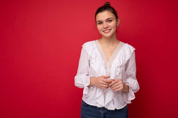 Retrato de mujer de moda alegre positiva en ropa formal sosteniendo dos manos juntas mirando a cámara aislada sobre fondo rojo con copia y espacio vacío.