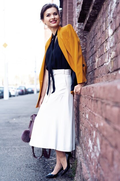 Retrato de mujer de moda caminando por la calle. Lleva chaqueta amarilla, sonriendo a un lado.