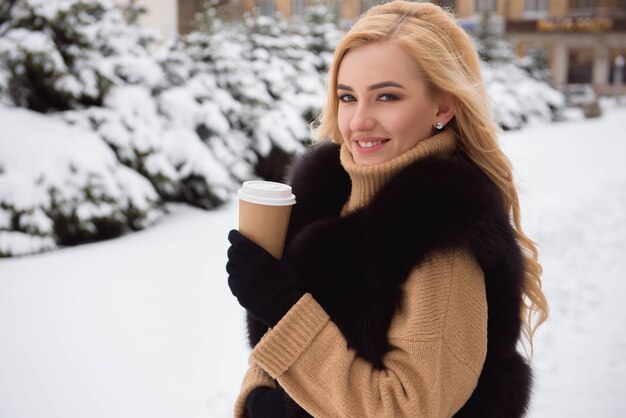 Retrato de mujer de moda de estilo europeo tomando café en el parque de invierno.