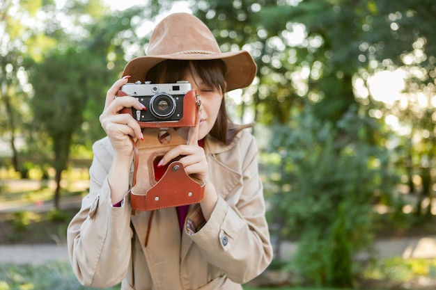 Retrato de mujer de moda joven con sombrero de fieltro con cámara retro en el parque de la ciudad