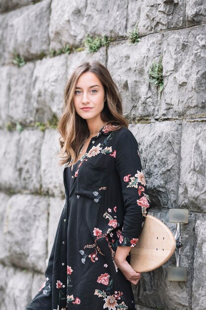 Retrato de mujer de moda con monopatín apoyado contra la pared