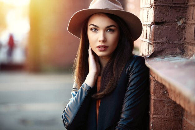 Retrato de mujer de moda de primer plano de joven muy de moda posando en la ciudad, moda callejera de otoño, sosteniendo el sombrero fedora retro popular hasta los años 60. riendo y sonriendo retrato de moda.