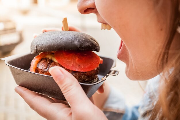 Retrato de mujer mordiendo hamburguesa negra con carne de vacuno de mármol