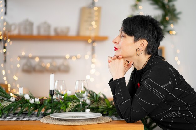 Retrato de mujer morena adulta con estilo haciendo un deseo de Navidad en la mesa.