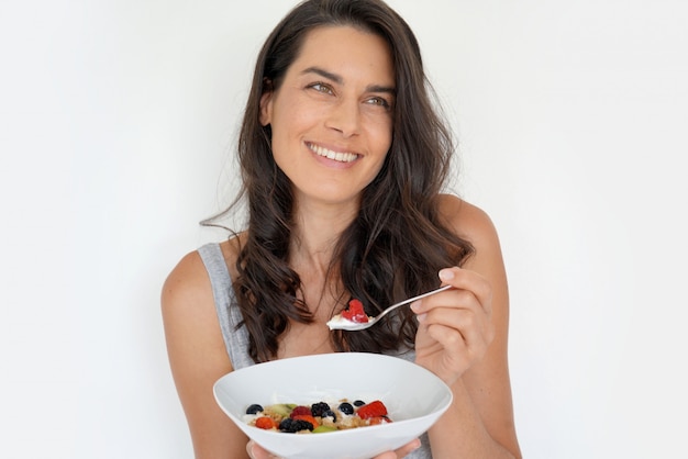 Retrato de la mujer morena atractiva que come el desayuno sano, aislado