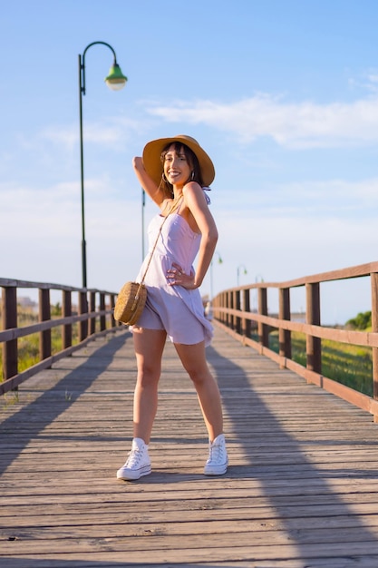 Retrato de mujer morena caucásica en la playa en vacaciones de verano caminando por una pasarela de madera