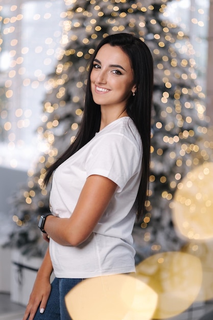 Retrato de mujer morena en chrisrmas time mujer atractiva parada junto a un gran árbol de navidad en frente