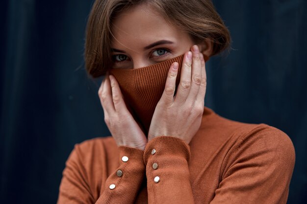 Retrato de mujer morena de confianza vestida de cuello alto marrón fondo oscuro atmósfera dramática Mujer caucásica headshoot estilo de suéter de golf de mujer