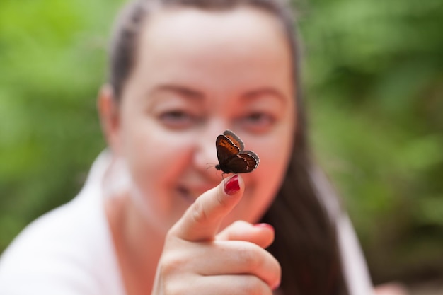 Retrato de una mujer morena feliz adulta sosteniendo mariposas en la mano en un claro del bosque y mostrando apaciguamiento psicológico