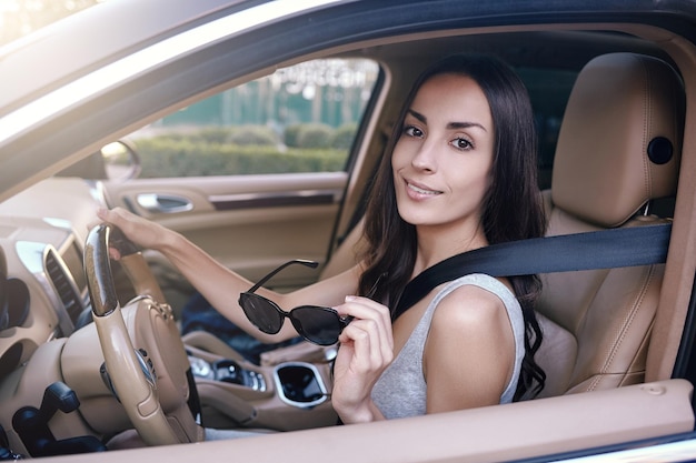 Retrato de mujer morena con gafas de sol y mirando a la cámara mientras está sentada en el auto
