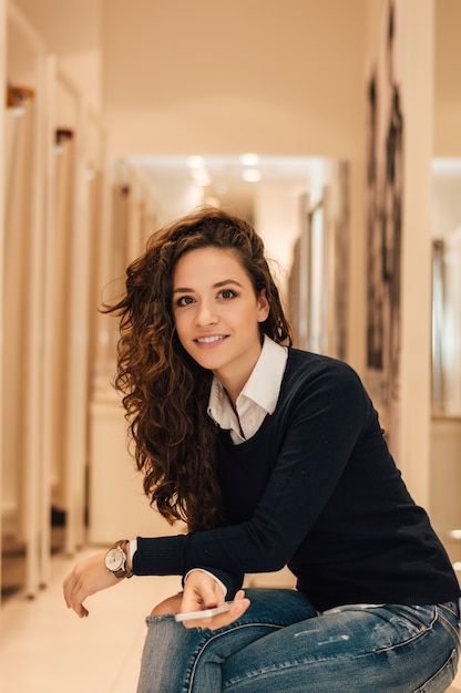 Retrato de la mujer morena hermosa que sostiene el teléfono en tienda de las compras.