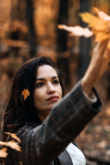 Retrato mujer morena con hojas amarillas caídas en cabello largo sobre fondo de naturaleza otoñal