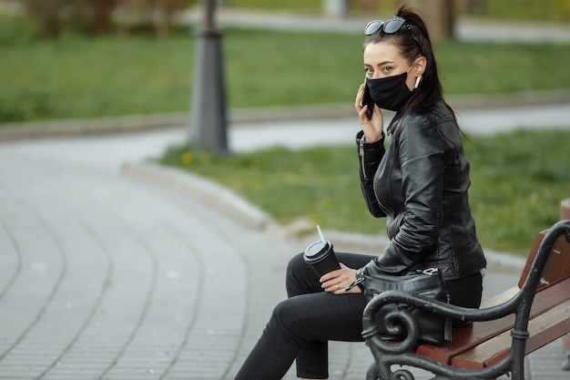 Retrato de mujer morena con una máscara protectora negra sentado en un banco en el parque