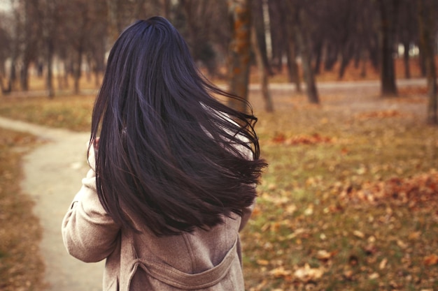 Retrato de mujer morena de pelo en abrigo beige caminando en el parque de la ciudad