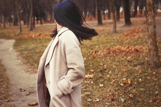 Retrato de mujer morena de pelo en abrigo beige caminando en el parque de la ciudad