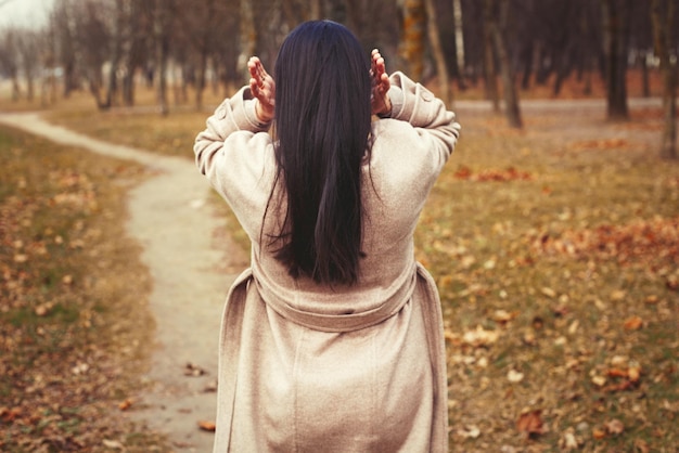 Retrato de mujer morena de pelo en abrigo beige caminando en el parque de la ciudad