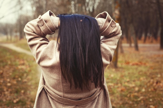 Retrato de mujer morena de pelo en abrigo beige caminando en el parque de la ciudad