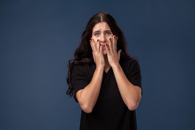 Retrato de una mujer morena de pelo largo en camiseta negra posando sobre un fondo gris y mostrando diferentes emociones.