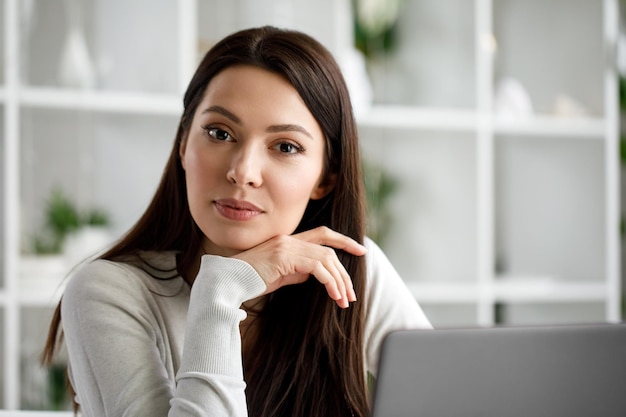 Retrato de una mujer morena que trabaja en una oficina con una computadora portátil Una mujer con una computadora portátil mira a la cámara y sonríe dulcemente