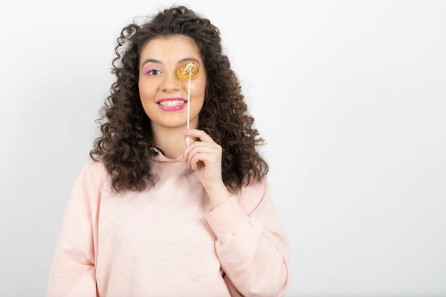 Retrato de mujer morena rizada con piruleta dulce delante de su ojo.