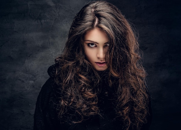 Retrato de mujer morena sensual con el pelo largo y rizado vestido con un jersey negro cálido.