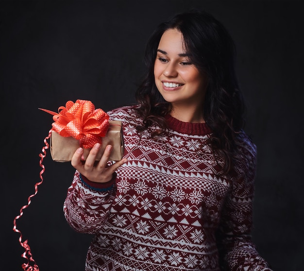 Retrato de mujer morena sonriente festiva con el pelo largo y rizado, vestida con un suéter rojo tiene regalos de Navidad.