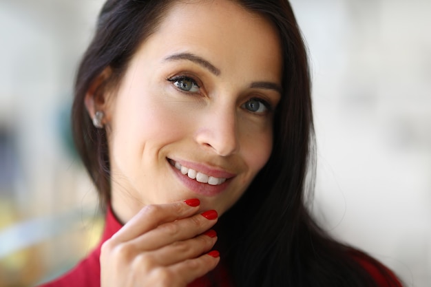 Retrato de mujer morena sonriente con manicura roja