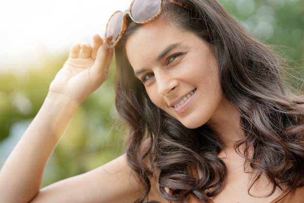 Foto retrato de la mujer morena sonriente que lleva las gafas de sol