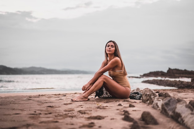 Retrato de una mujer morena con traje de baño en la playa en verano sentada en la arena