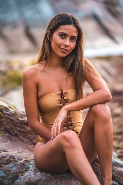 Retrato de una mujer morena con traje de baño en las rocas de la playa en verano mirando a la cámara