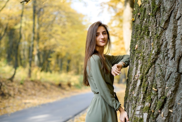 Retrato de mujer morena en vestido verde posando en el parque otoño