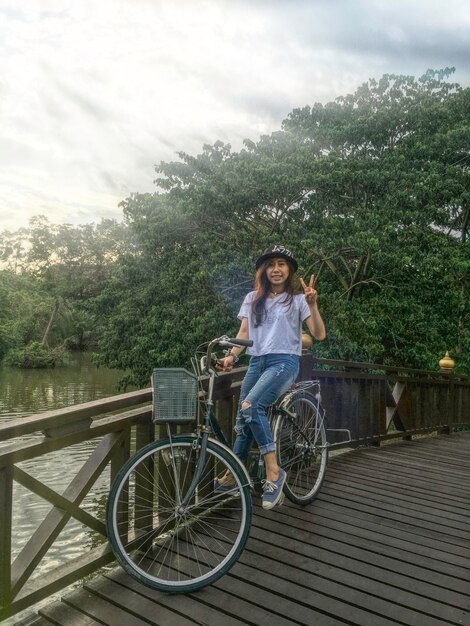 Foto retrato de una mujer mostrando un signo de paz mientras está sentada en una bicicleta en el puente