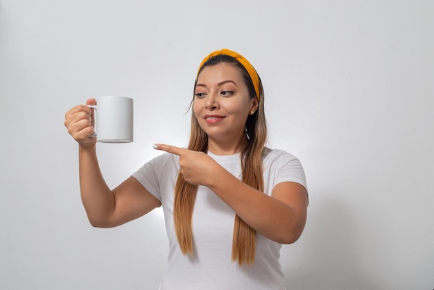 Retrato de mujer mostrando una taza blanca Persona sosteniendo una taza de café fondo blanco.