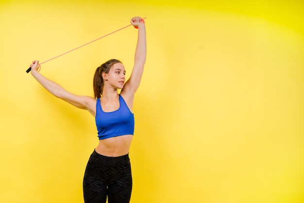 Retrato de una mujer musculosa y suave con una cuerda para saltar en el cuello aislada sobre un fondo amarillo