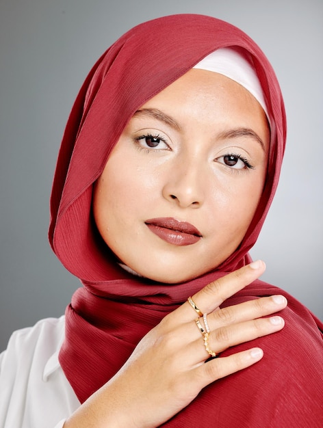 Retrato de mujer musulmana con estilo con maquillaje y anillos de oro aislados contra un fondo gris Edgy joven hijab sintiéndose confiada en su bufanda roja y bisutería de moda Modestia y belleza