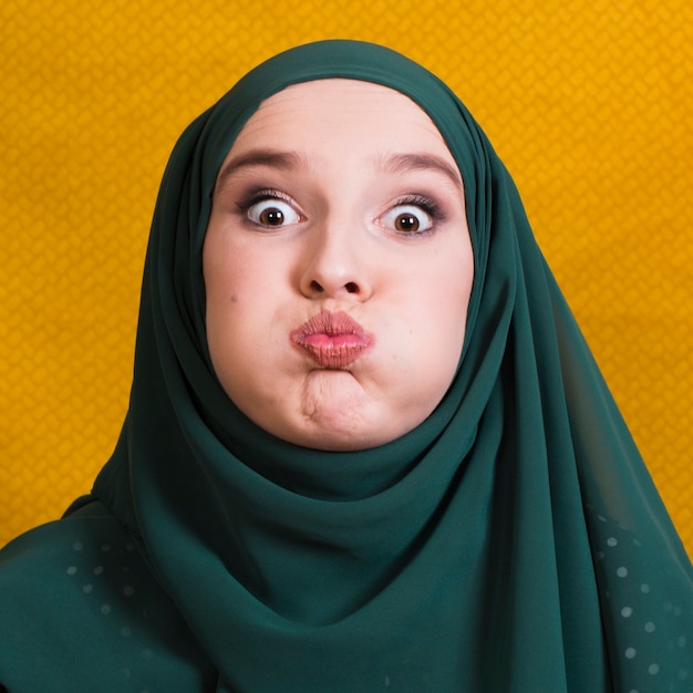 Retrato de una mujer musulmana haciendo una expresión facial divertida frente a un fondo amarillo