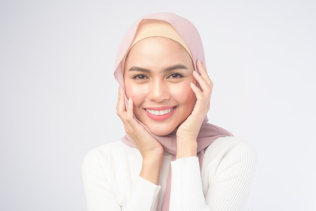 Un retrato de una mujer musulmana sonriente joven que lleva un hijab rosado en blanco.