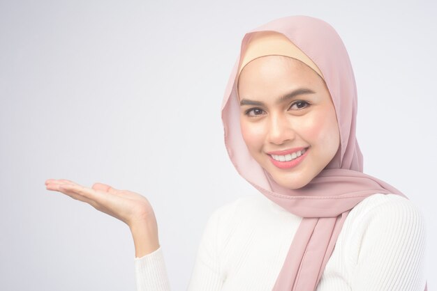 Un retrato de una mujer musulmana sonriente joven que lleva un hijab rosado sobre el estudio del fondo blanco.