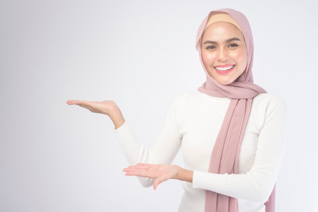 Un retrato de una mujer musulmana sonriente joven que lleva un hijab rosado sobre el estudio del fondo blanco.