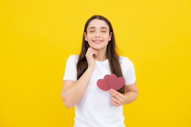 Retrato de mujer muy sonriente sosteniendo corazón de papel en sus manos sobre fondo amarillo Concepto de amor