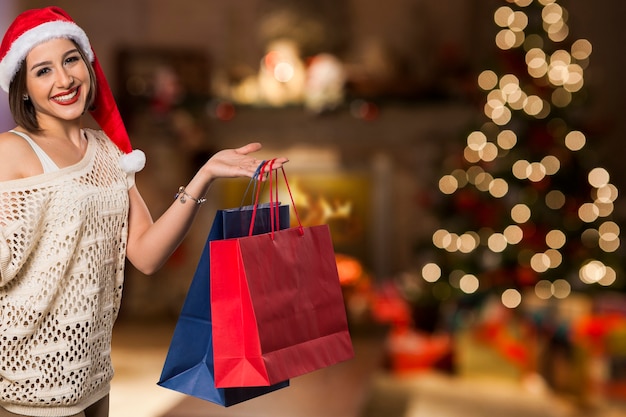 Retrato de mujer de Navidad con bolsas de la compra. Sonriente mujer feliz sobre luces de Navidad bokeh