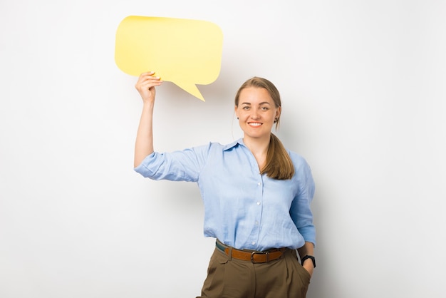 Retrato de mujer de negocios alegre vistiendo camisa azul y sosteniendo bocadillo de diálogo en blanco amarillo