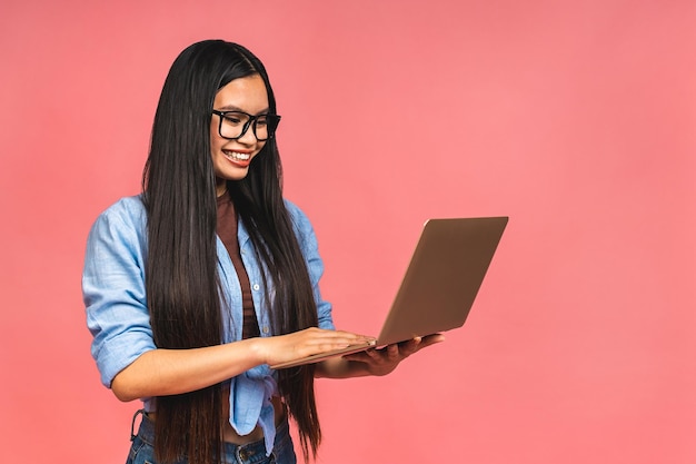 Retrato de una mujer de negocios asiática feliz trabajando en una laptop aislada de fondo rosa